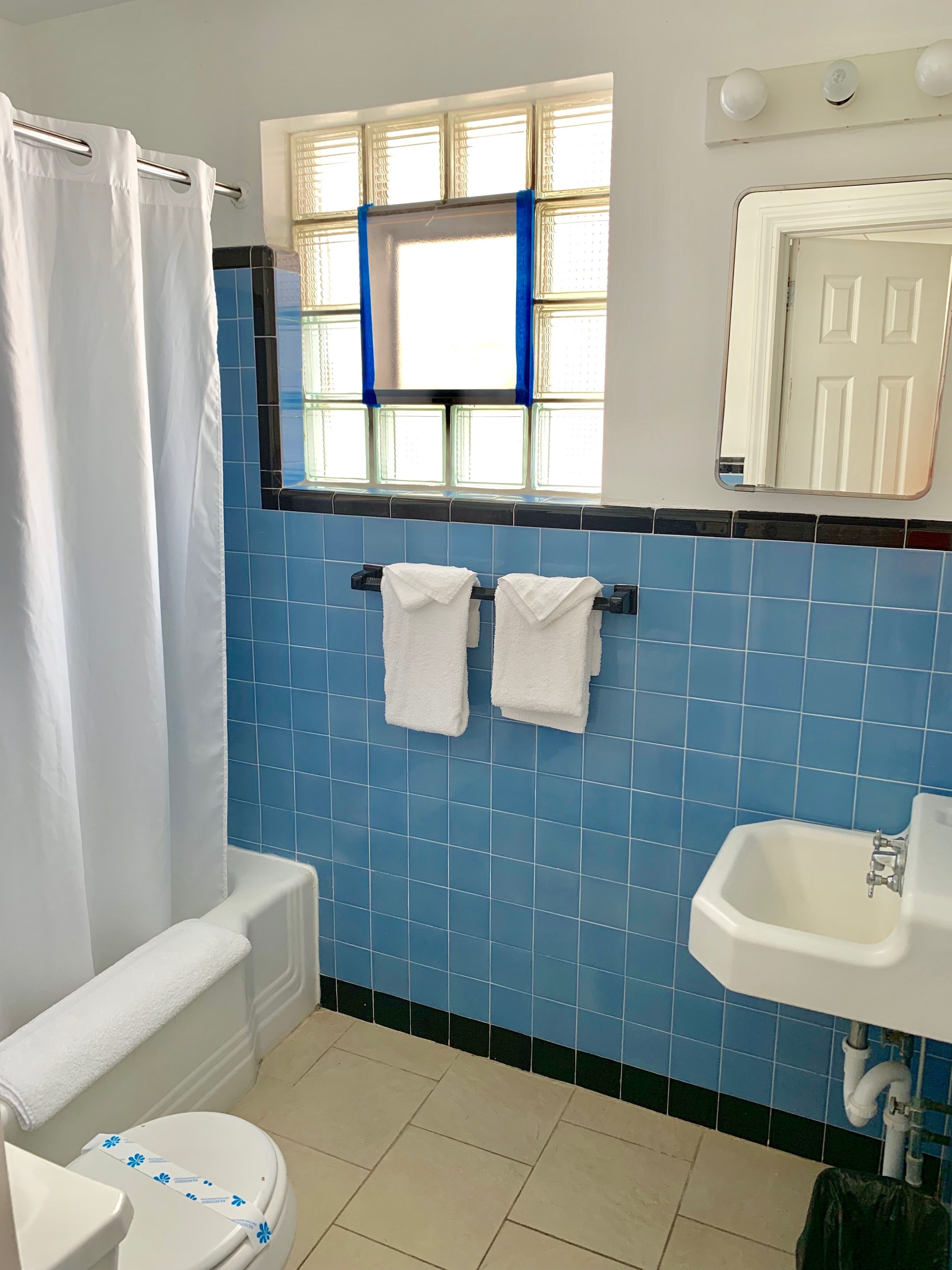 A bathroom with blue tiles, a white toilet, a white sink, and a window with blue curtains.