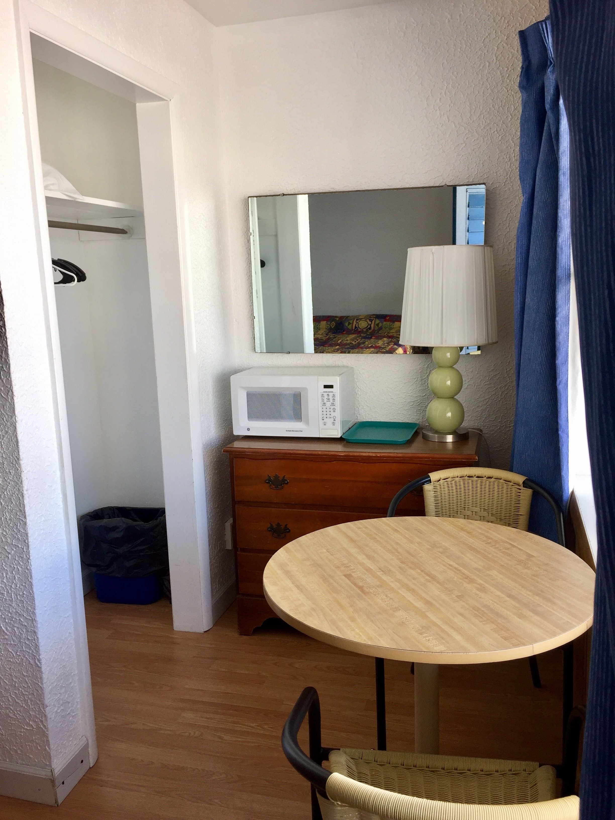 Una habitación pequeña con un aparador de madera, un microondas, una mesa, una silla de mimbre y una cortina azul.