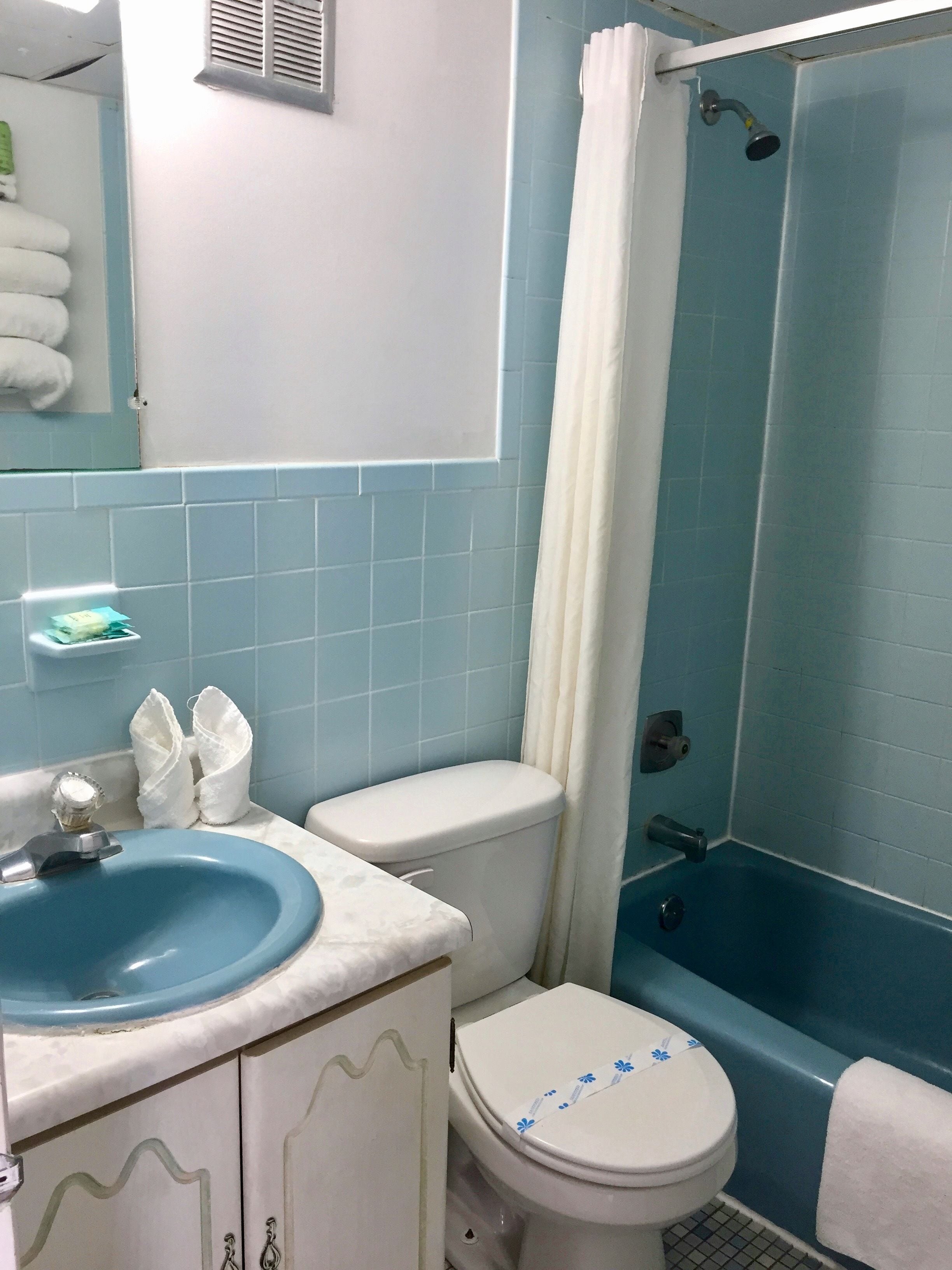 Ein Badezimmer mit blauen Fliesen, einer weißen Toilette, einem blauen Waschbecken und einer Duschkabine.
