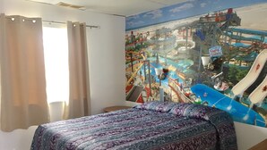 Quarto de hotel com cama, janela com cortinas e um mural de parque aquático.