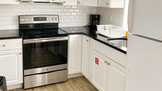 Uma cozinha moderna com armários brancos, forno de aço inoxidável, micro-ondas e geladeira.