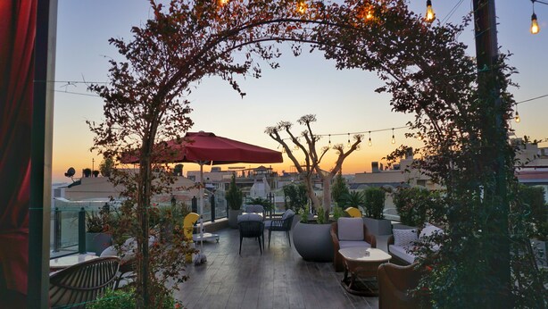 An outdoor seating area with tables and chairs, a red umbrella, and string lights.