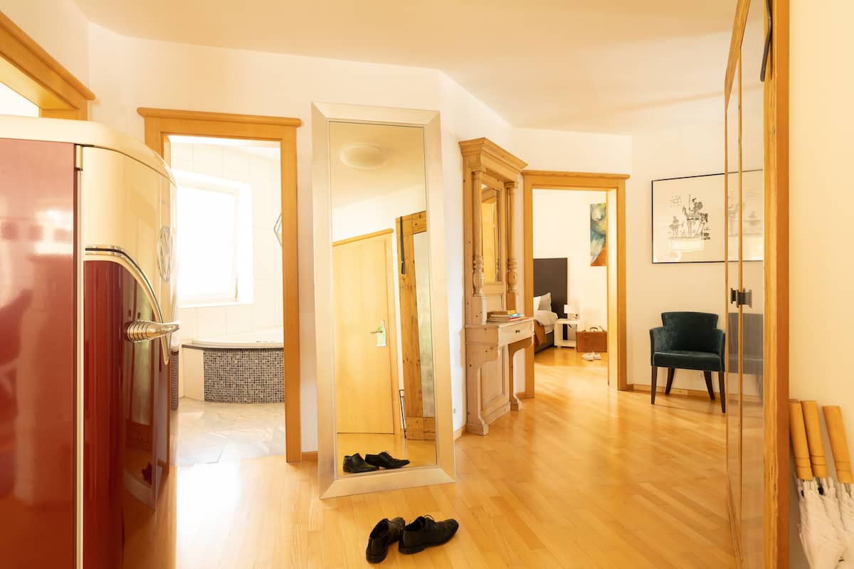 A spacious room with a wooden floor, a mirror, a red refrigerator, and a chair.