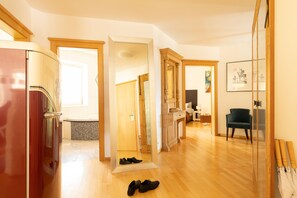 A spacious room with a wooden floor, a mirror, a red refrigerator, and a chair.