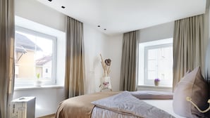 A bedroom with a bed, a suitcase, a window, and a view of buildings outside.