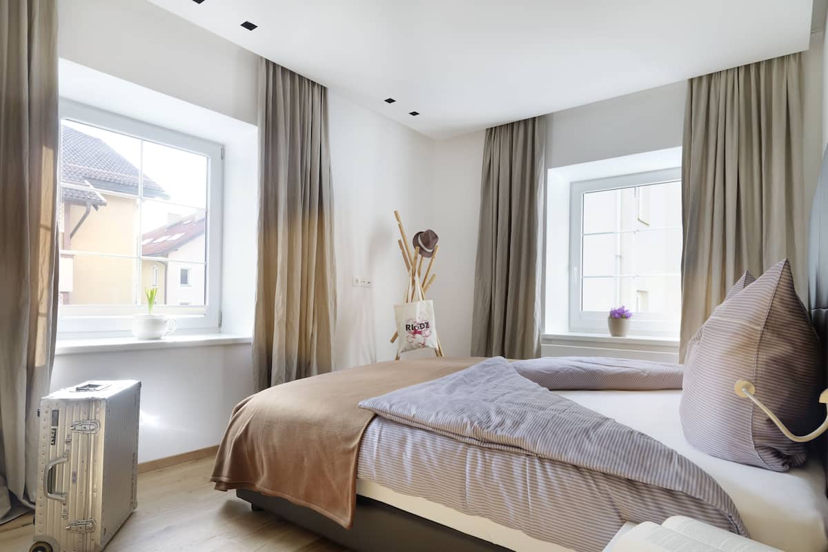 A bedroom with a bed, a suitcase, a window, and a view of buildings outside.