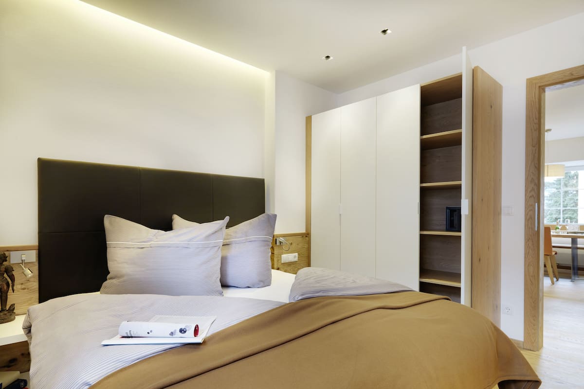 A modern bedroom with a large bed, a wooden wardrobe, and a desk with a chair.