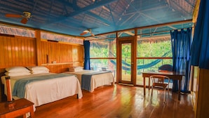 A room with two beds, a wooden floor, a ceiling fan, and a view of greenery outside. - Muyuna Lodge (Fernando Lores)