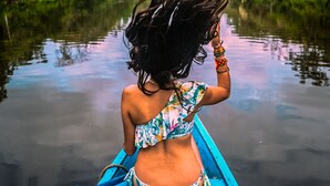 A person in a boat on a calm river, surrounded by lush greenery and a cloudy sky.