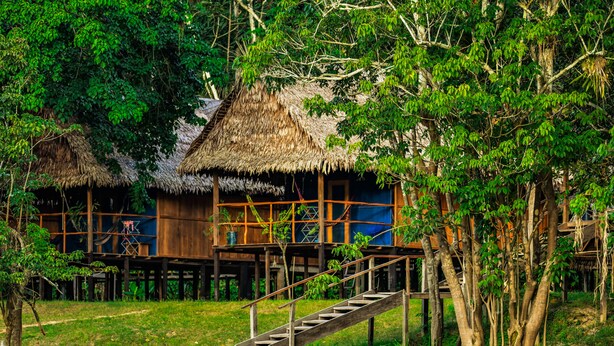 A traditional wooden house with a thatched roof, surrounded by lush greenery. - Muyuna Lodge (Fernando Lores)