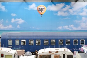 Un tren azul con múltiples ventanales y un globo aerostático con el texto 'base camp' en el cielo.