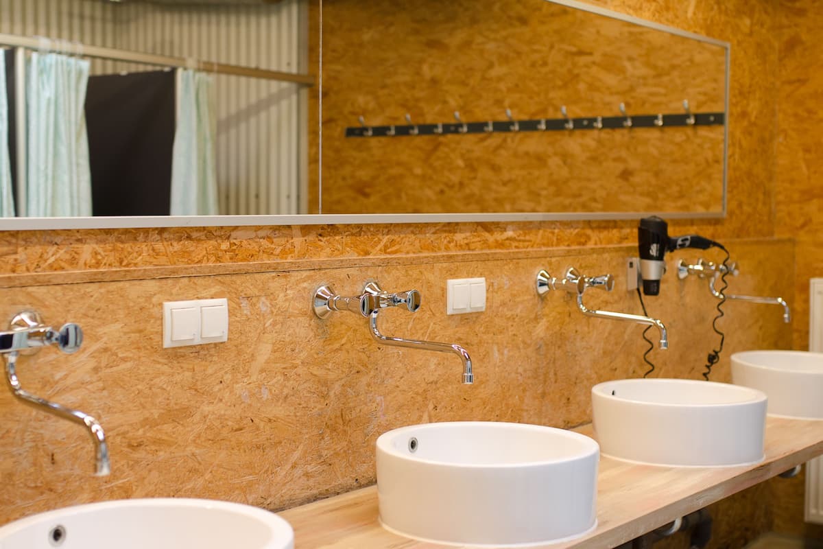 A bathroom with three sinks, a mirror, and a towel rack.