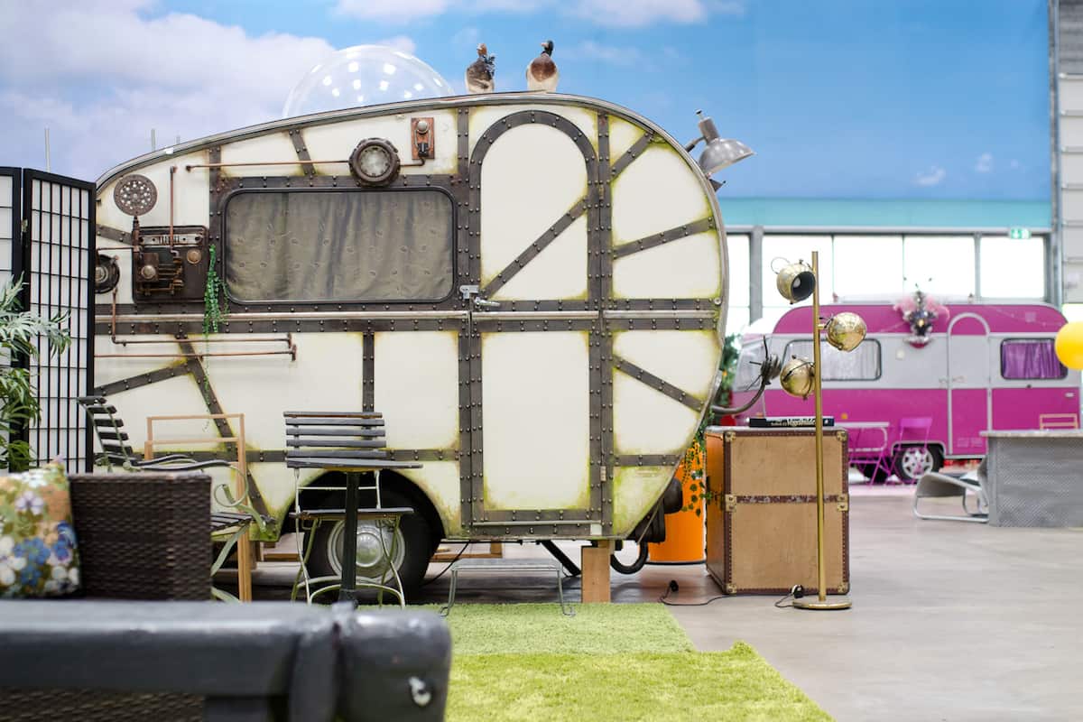 A vintage camper with a rustic design, featuring a large window, a small kitchen area, and a sleeping berth.