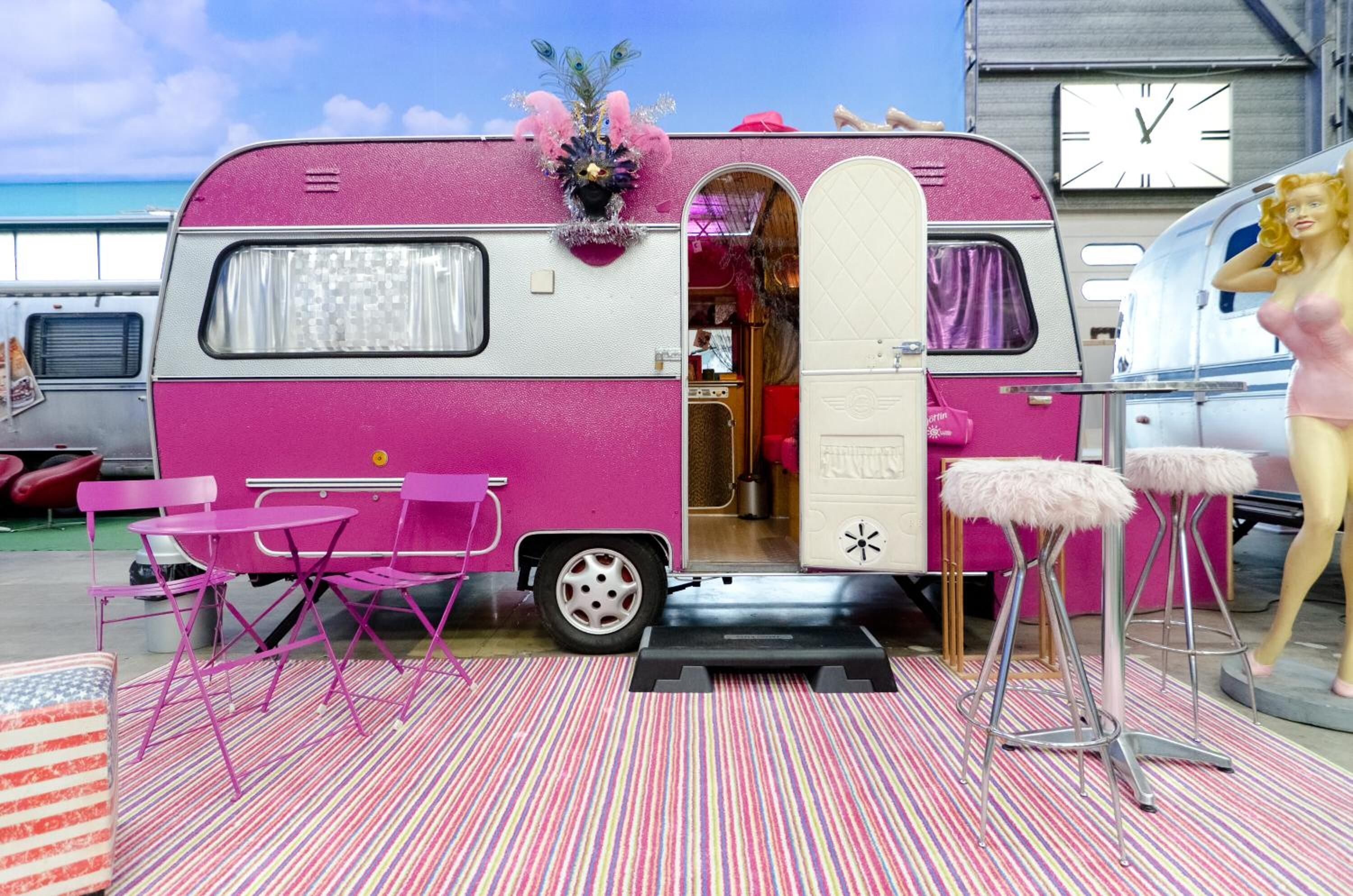 Una caravana rosa con un interior pequeño, sillas rosas y un maniquí.