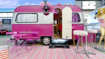 Una caravana rosa con un interior pequeño, sillas rosas y un maniquí.