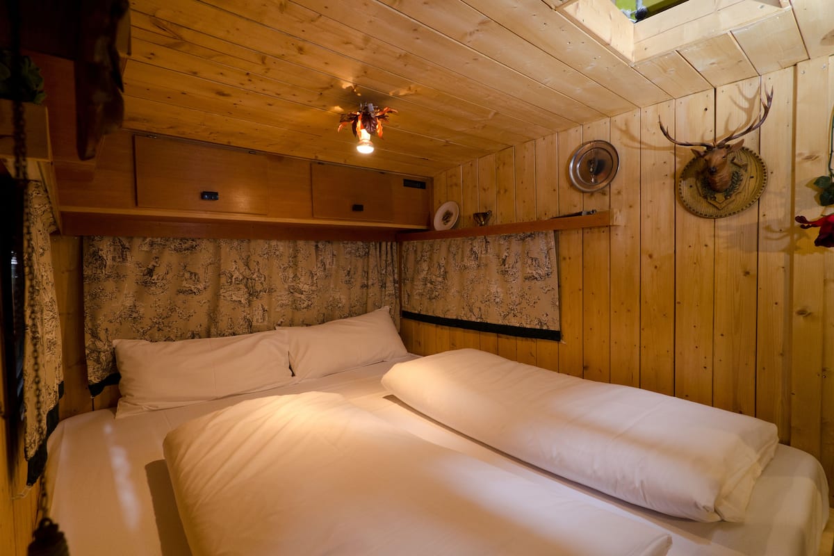 A wooden cabin room with two beds, a ceiling light, and a wall-mounted hat.