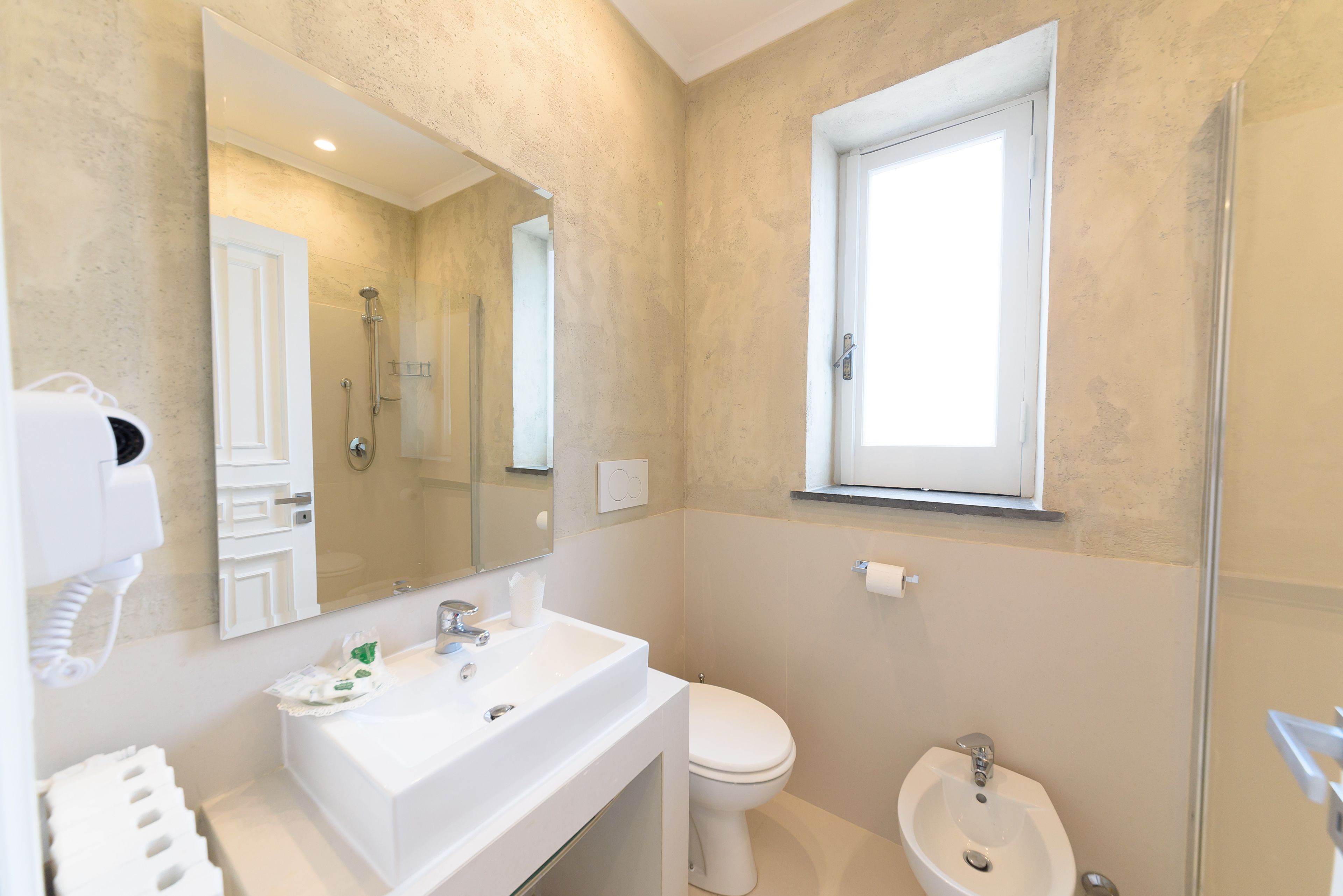Un baño con lavamanos blanco, inodoro, bidé, espejo y ventana.