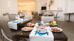 A breakfast setting with wicker chairs, a dining table with plates of food, a coffee cup, and a television on a shelf. - Villa Fortuna Holiday Resort (Ischia)