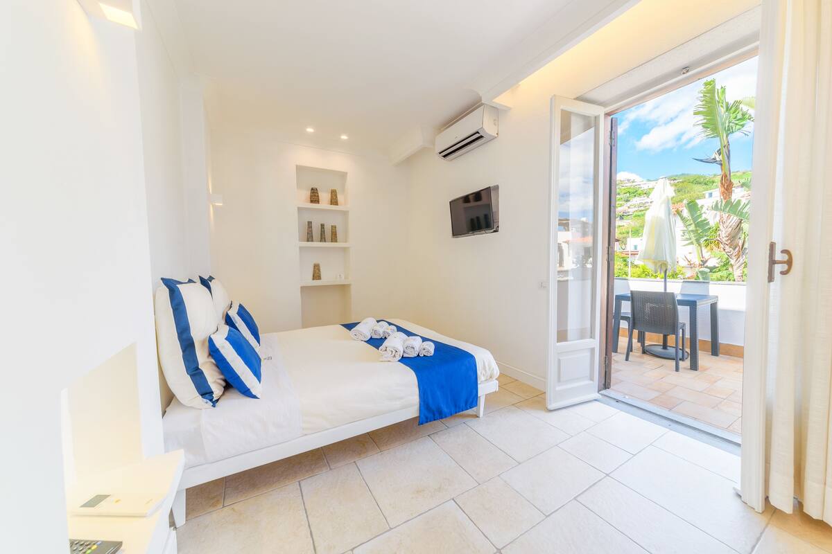 A bedroom with a bed, a TV, a shelf with decorative items, and a view of the outside patio.
