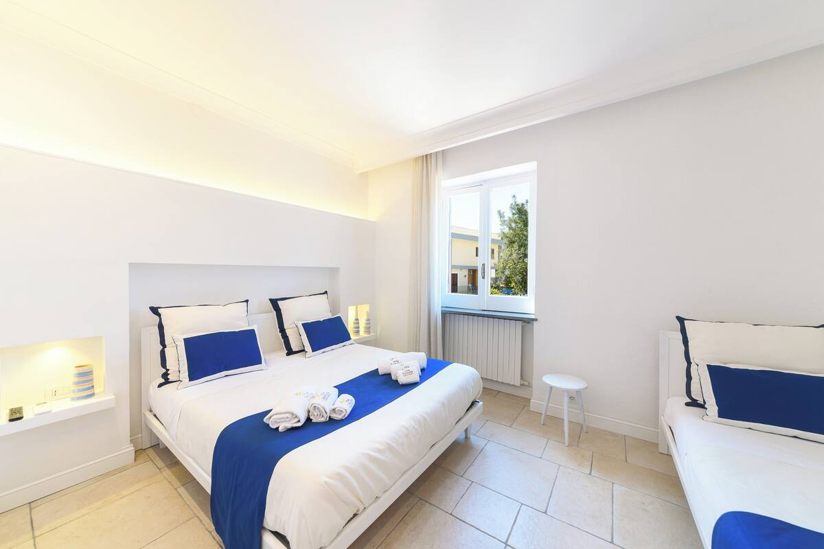A modern hotel room with a large bed, a small bedside table, a window with a view, and a white radiator.