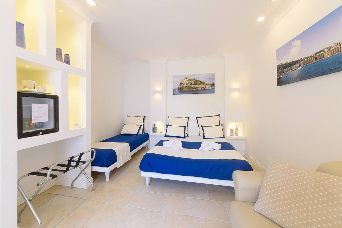 A hotel room with two beds, a small table, a chair, a TV, and artwork on the walls.