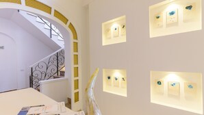 A hotel lobby with a staircase, a reception desk, and wall-mounted light fixtures. - Villa Fortuna Holiday Resort (Ischia)