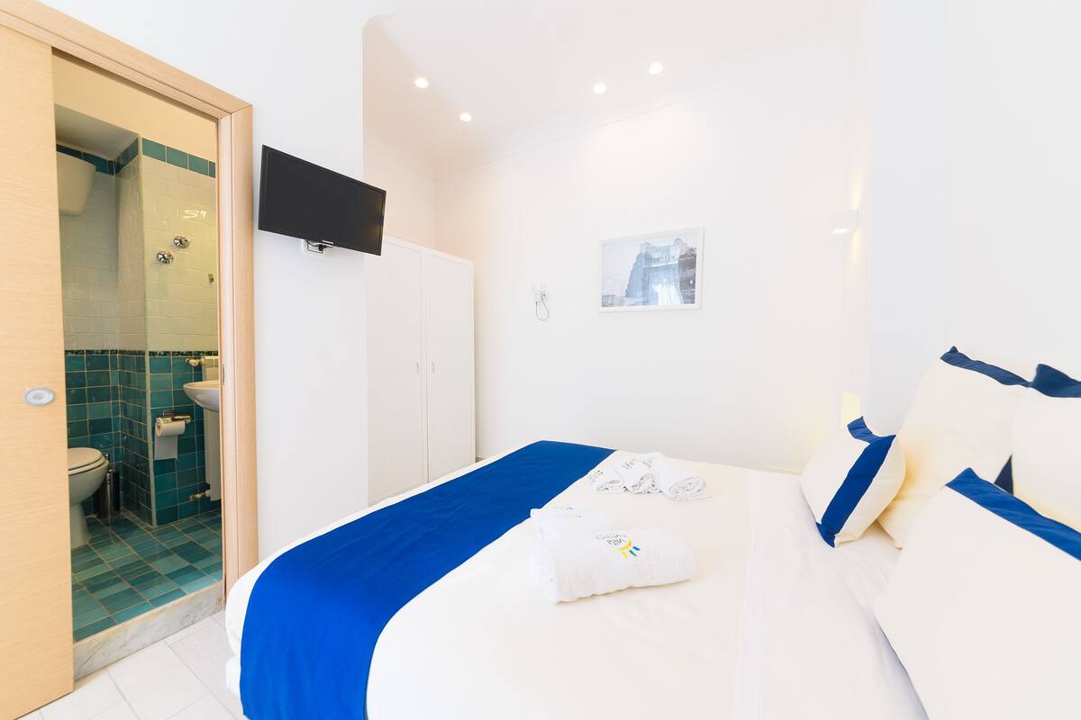 A hotel room with a bed, a bathroom, a TV, and a picture on the wall.
