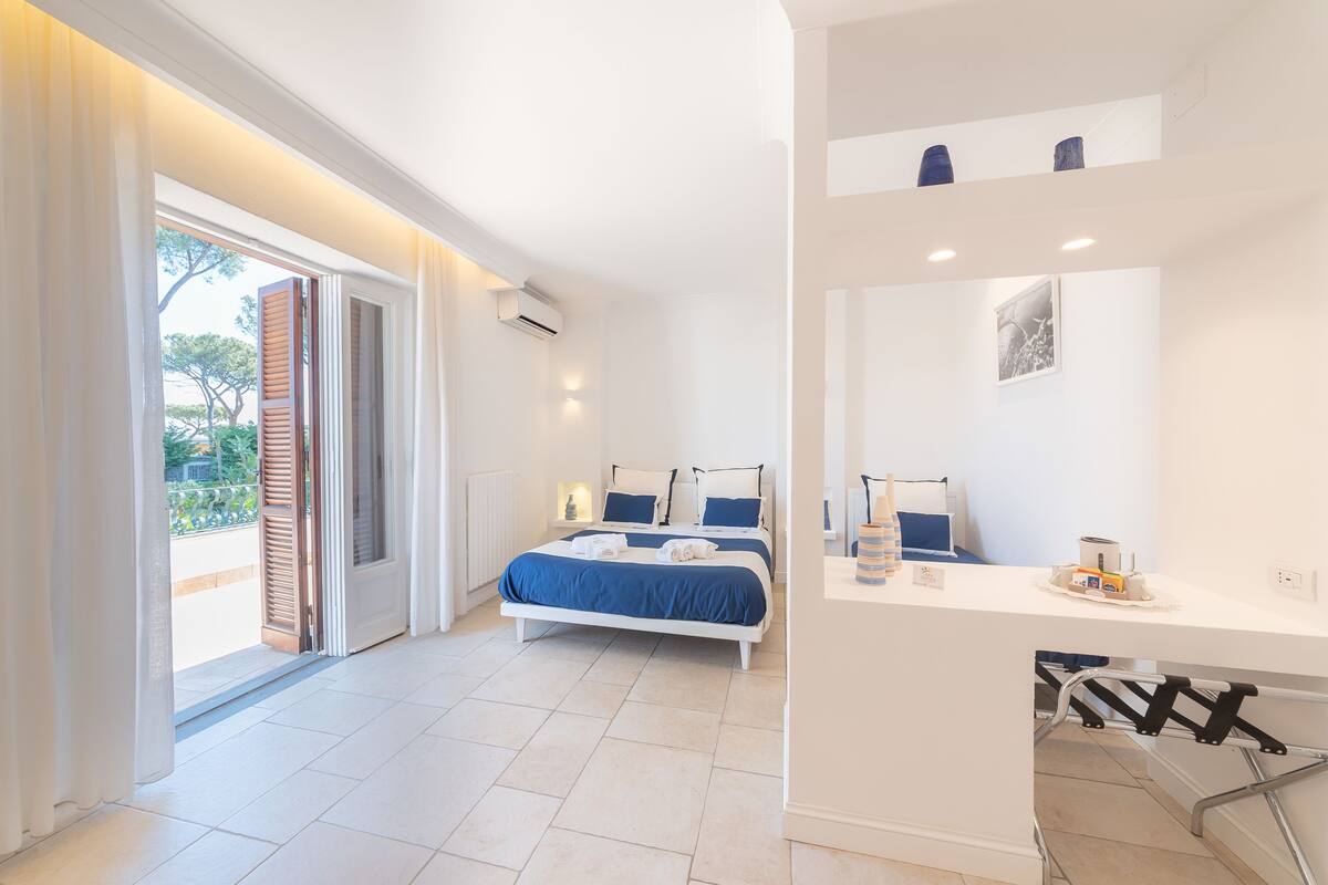A bedroom with a bed, a desk, a chair, and a balcony.