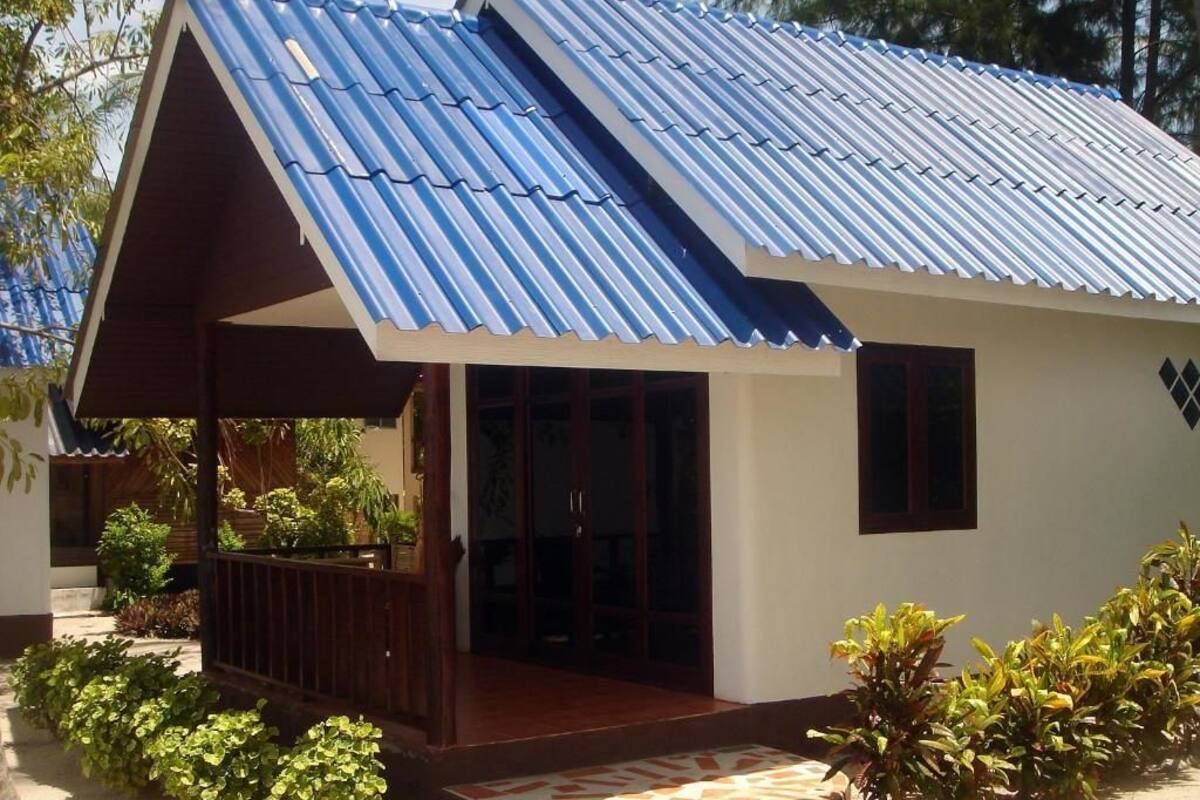 Una casita con techo azul metálico inclinado, un porche de madera y entrada con baldosas.
