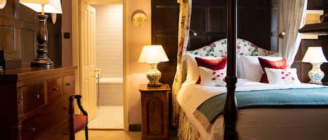 Una cama con dosel adornada con ropa de cama floral, un aparador de madera y dos lámparas de noche.