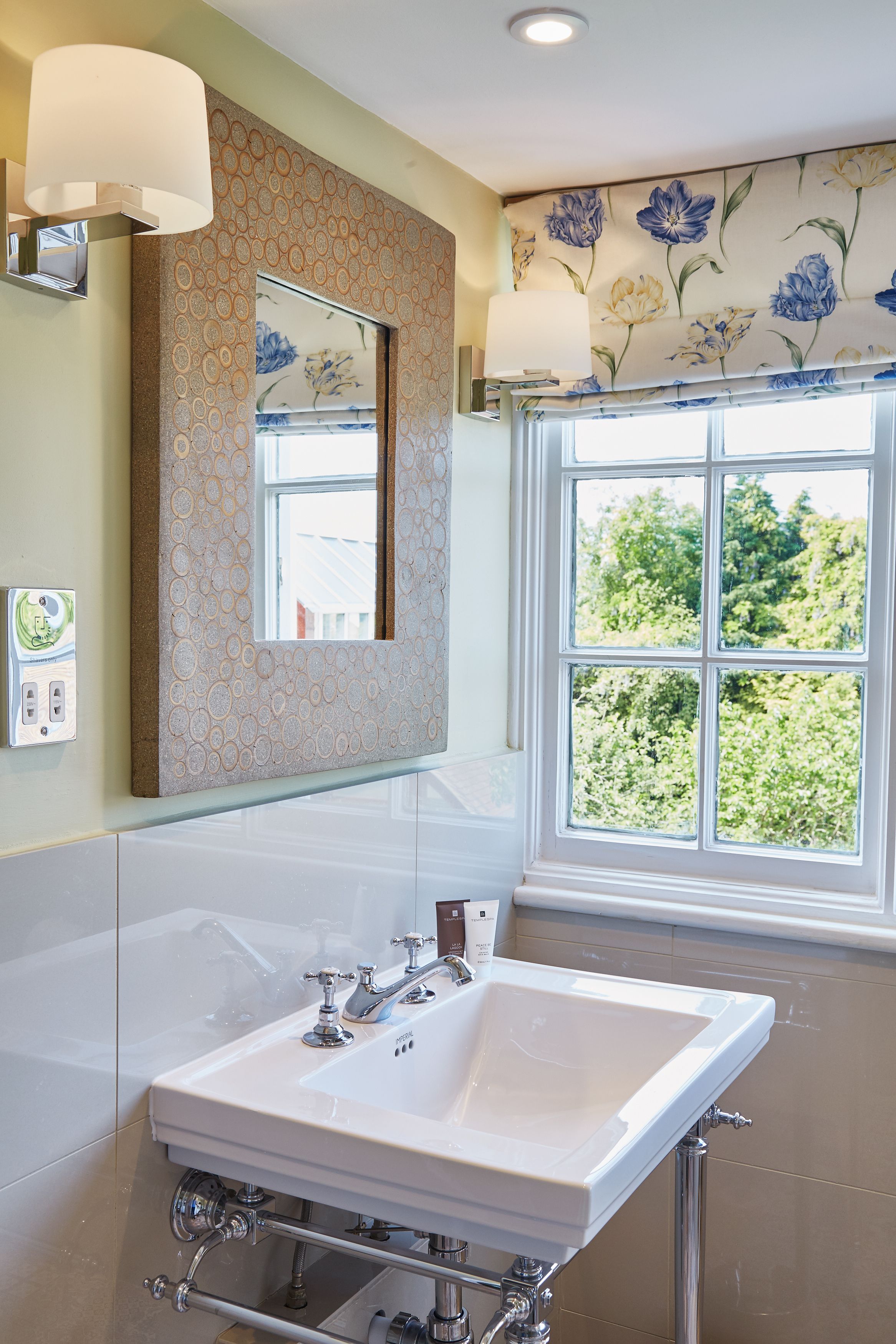 A bathroom with a large mirror, a sink, and a window with a view of greenery.