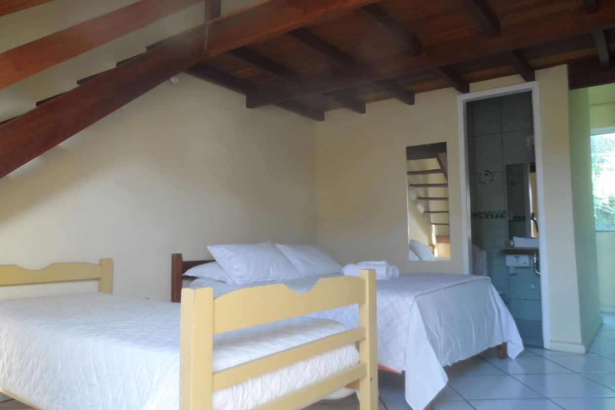 Un dormitorio con dos camas individuales, techo de madera y un baño visible a través de una puerta abierta.