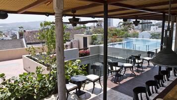 A rooftop terrace with a pool, outdoor seating, and a view of the cityscape.