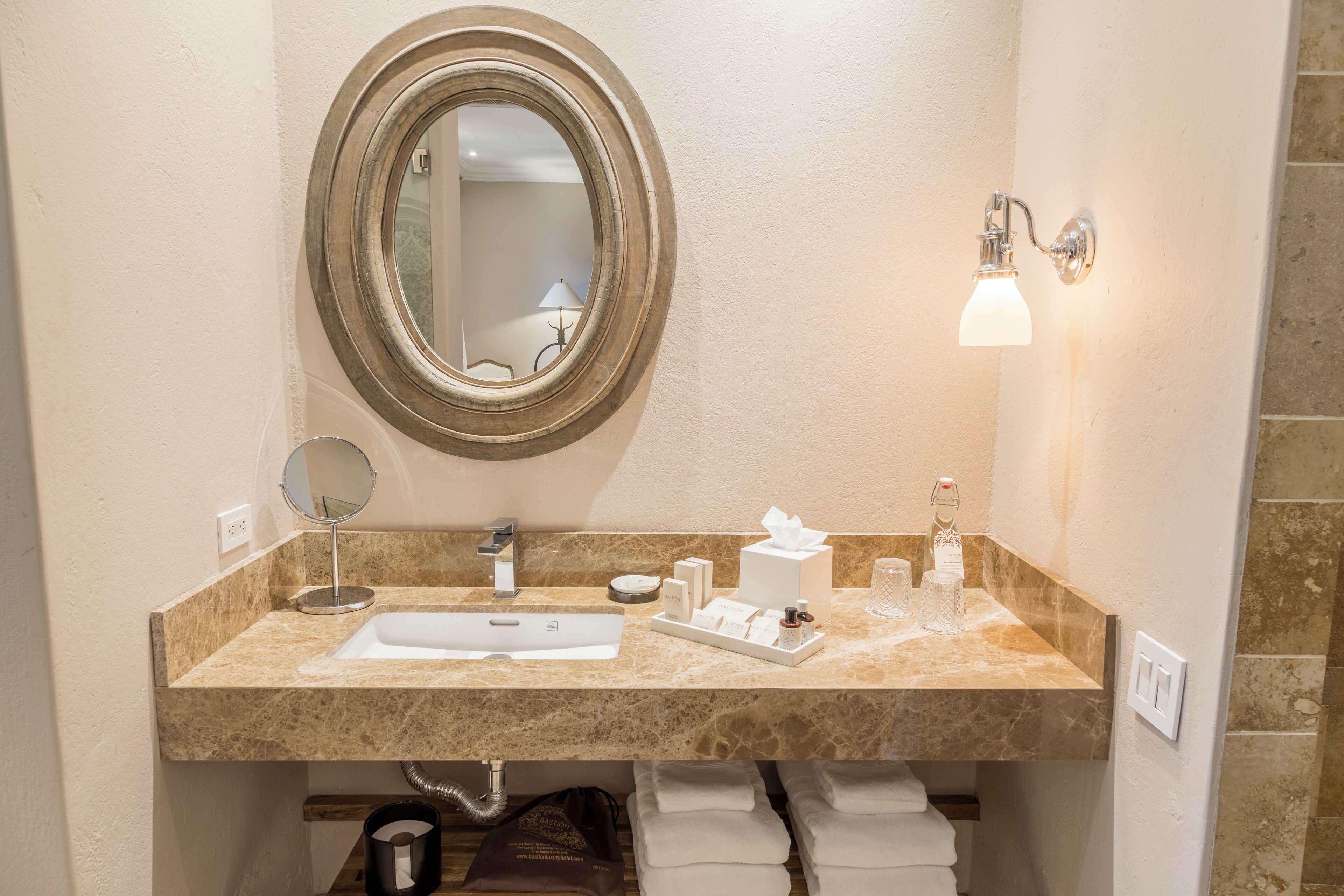 Un baño con lavamanos de mármol, un espejo redondo, un perchero y un aplique de pared.