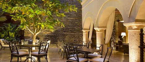 An outdoor dining area with stone walls and arches, featuring tables and chairs arranged for guests.