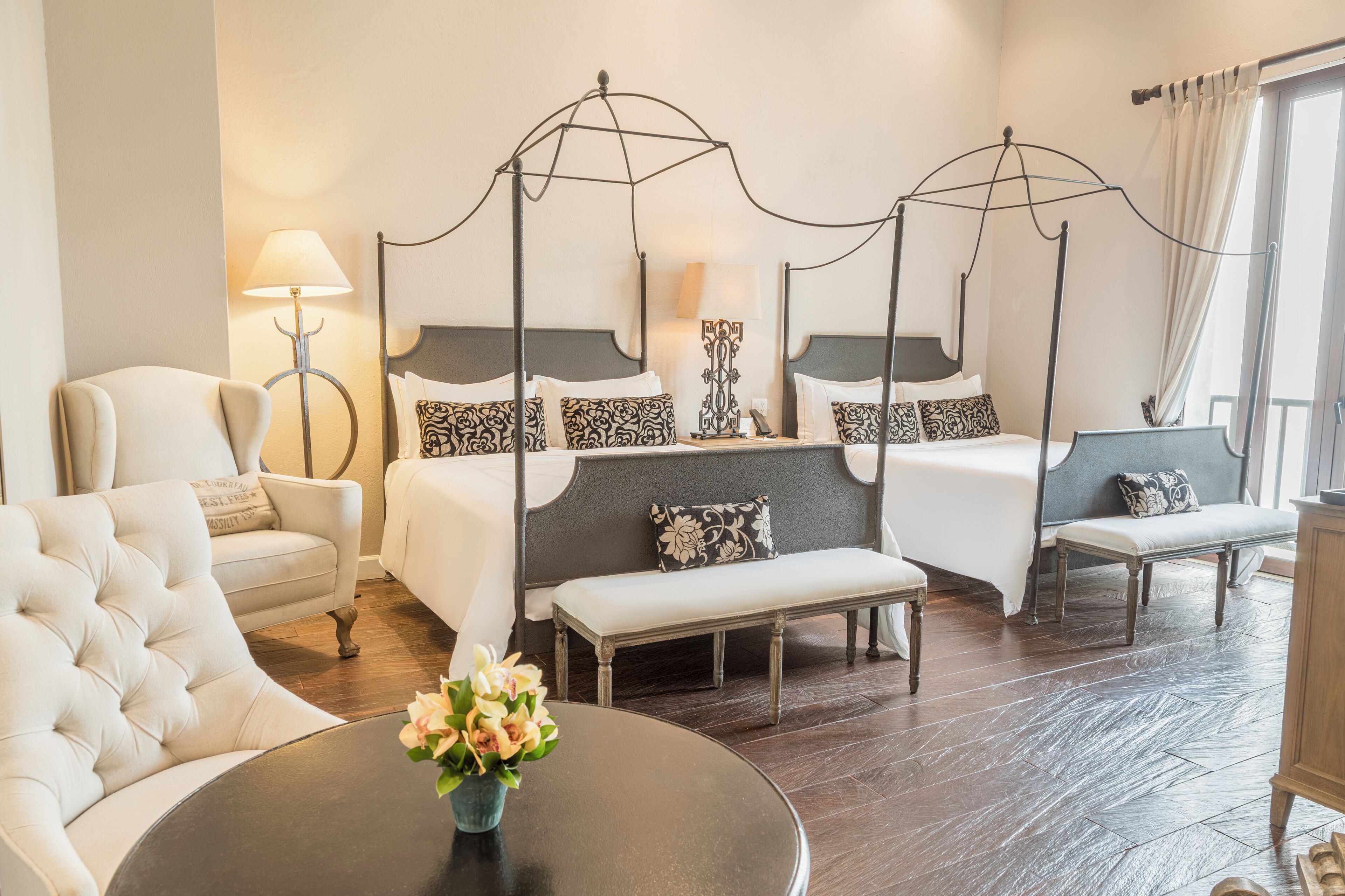 A hotel room with a four-poster bed, a sofa, a bench, and a round table with a vase of flowers.