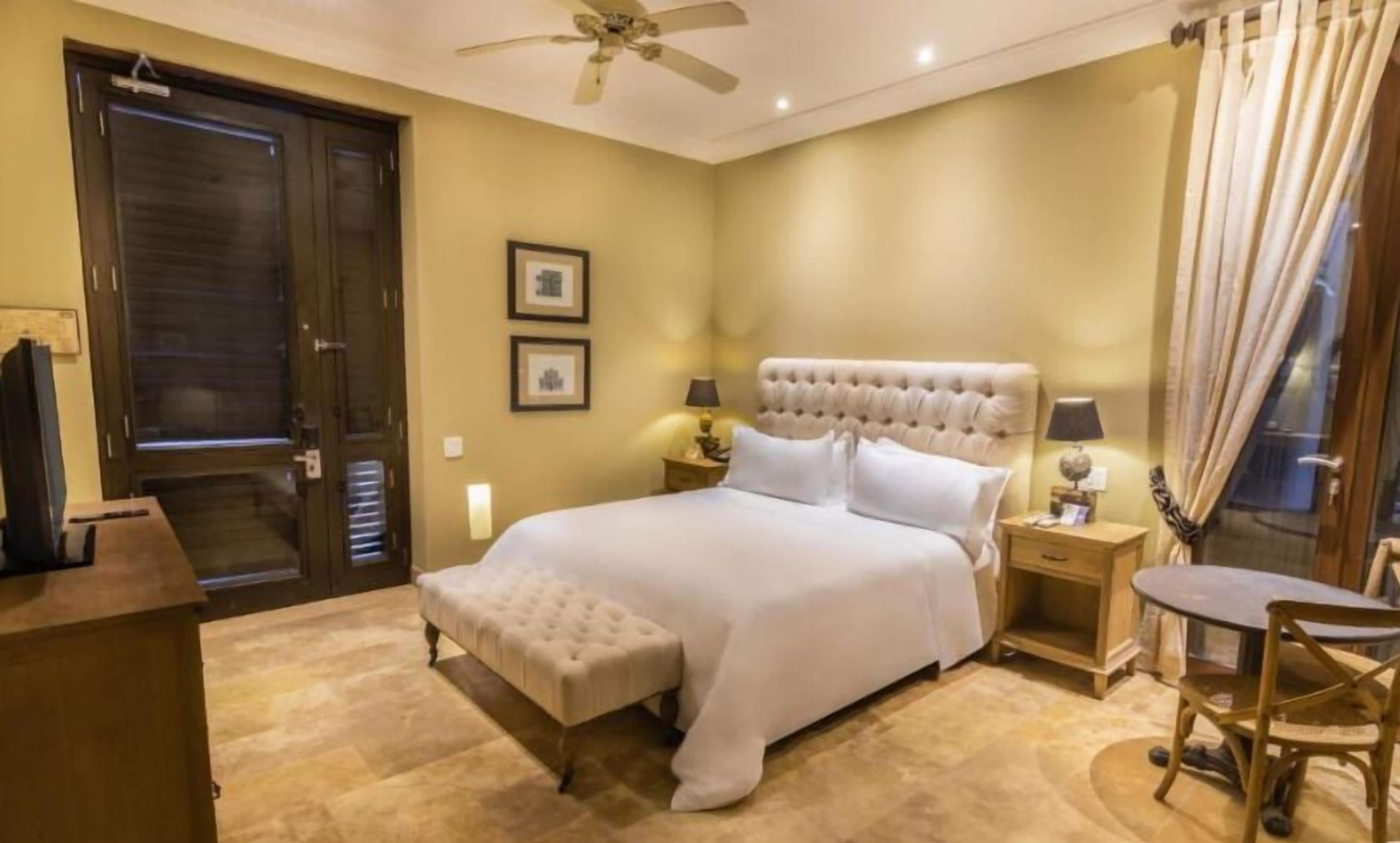 Habitación de hotel con una cama grande, un escritorio, una silla, un ventilador de techo y dos cuadros en la pared.