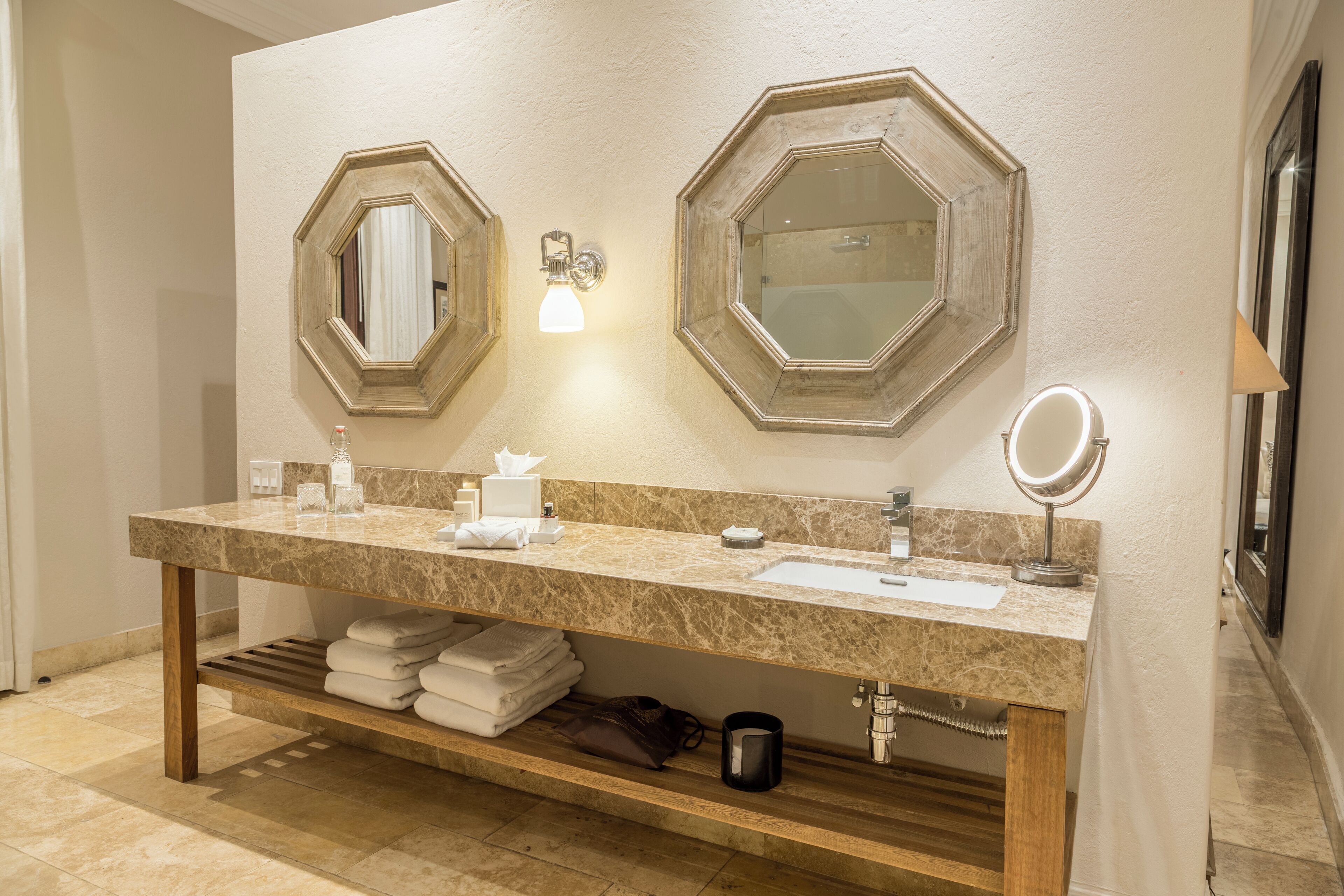 Un baño con tocador de mármol, dos espejos, un perchero y un lavabo.