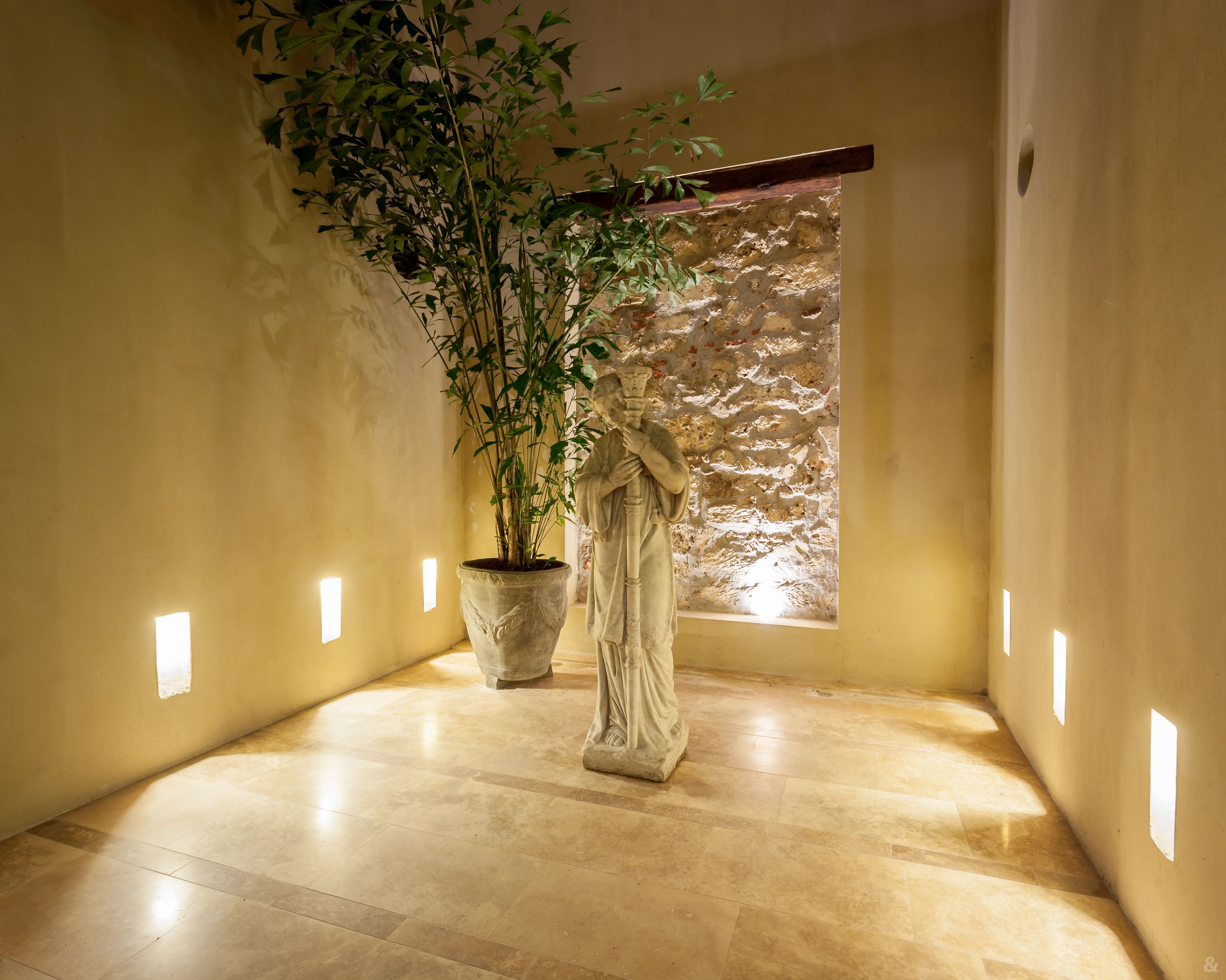 A hallway with a statue, a potted plant, and a stone wall.