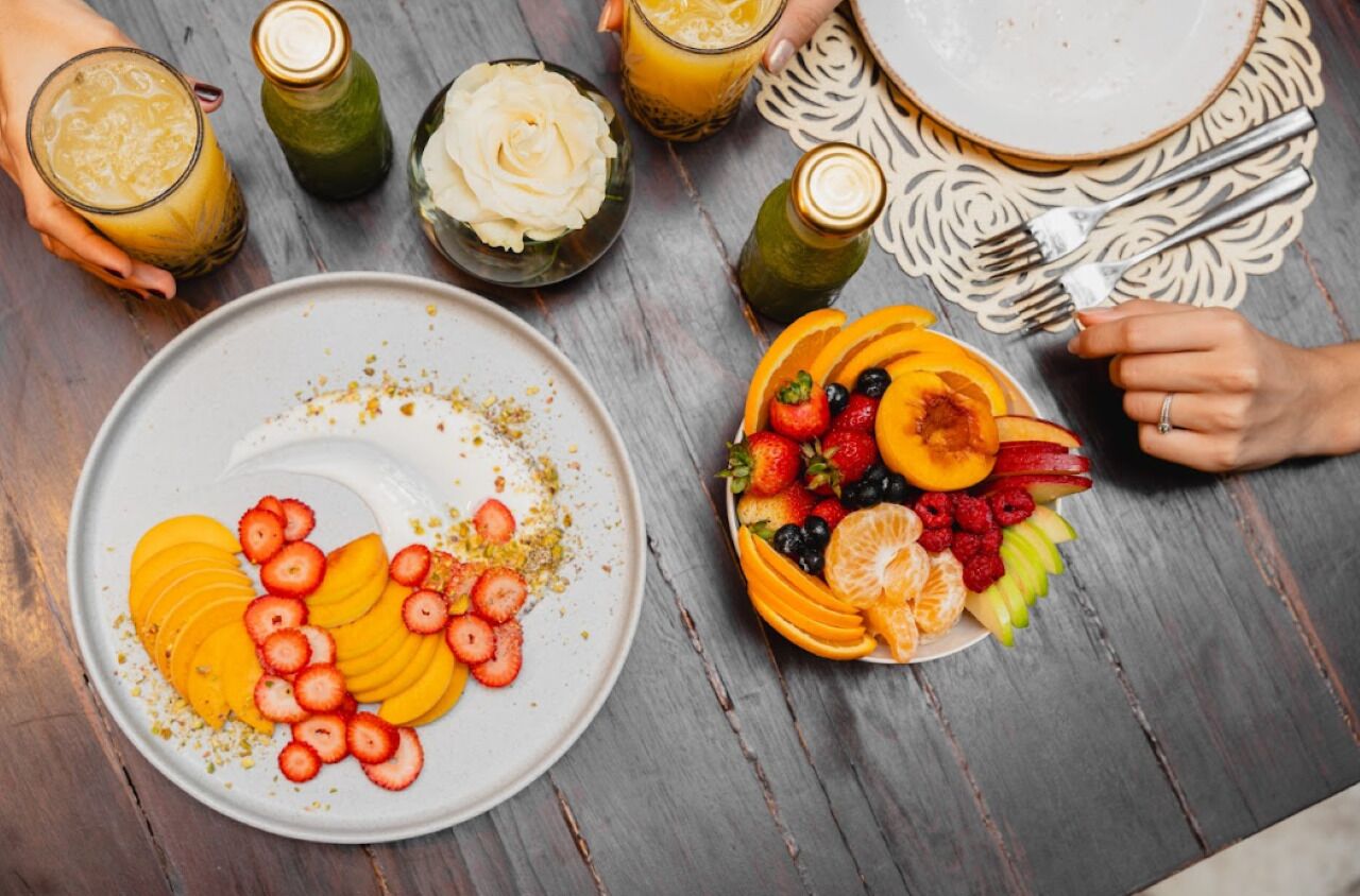 Una mesa con un plato de frutas cortadas y un vaso de jugo.