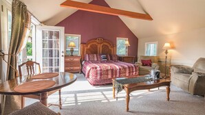 A bedroom with a sloped ceiling, a bed with a patterned bedspread, a wooden nightstand, a bedside table with lamps, and a window with curtains. - White Rose Inns (Wisconsin Dells)