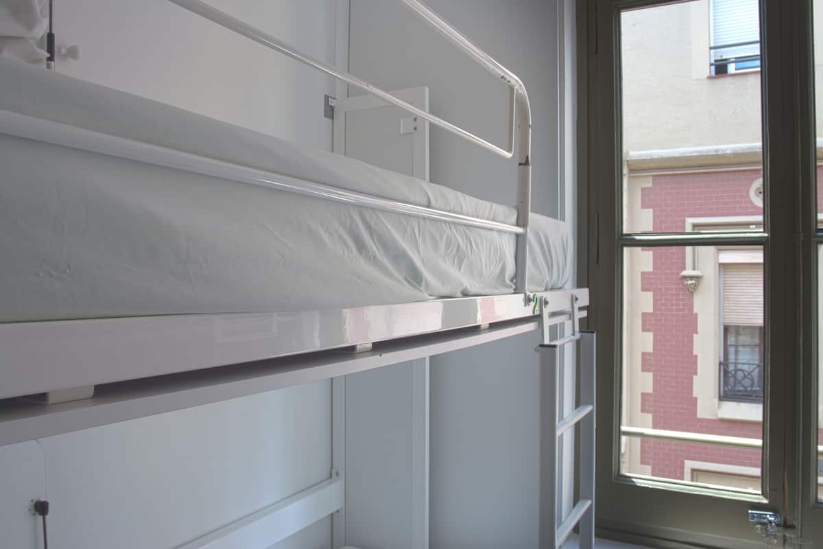 Uma cama de beliche com escada de metal e janela com vista para um edifício.