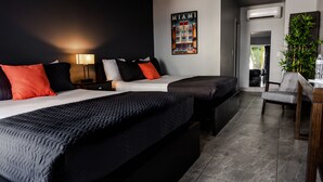 Ett hotellrum med två sängar, ett skrivbord, en stol, en krukväxt och en väggmonterad luftkonditioneringsanläggning.