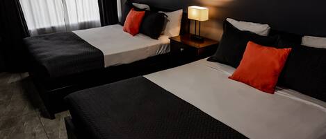 Ett hotellrum med två sängar, båda med svartvita sängkläder och röda kuddar. Mellan sängarna står ett nattduksbord med en lampa.