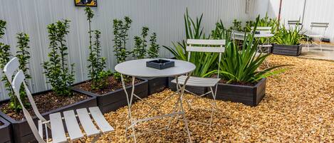 A patio area with a round table, two white chairs, a bench, and a planter with plants.