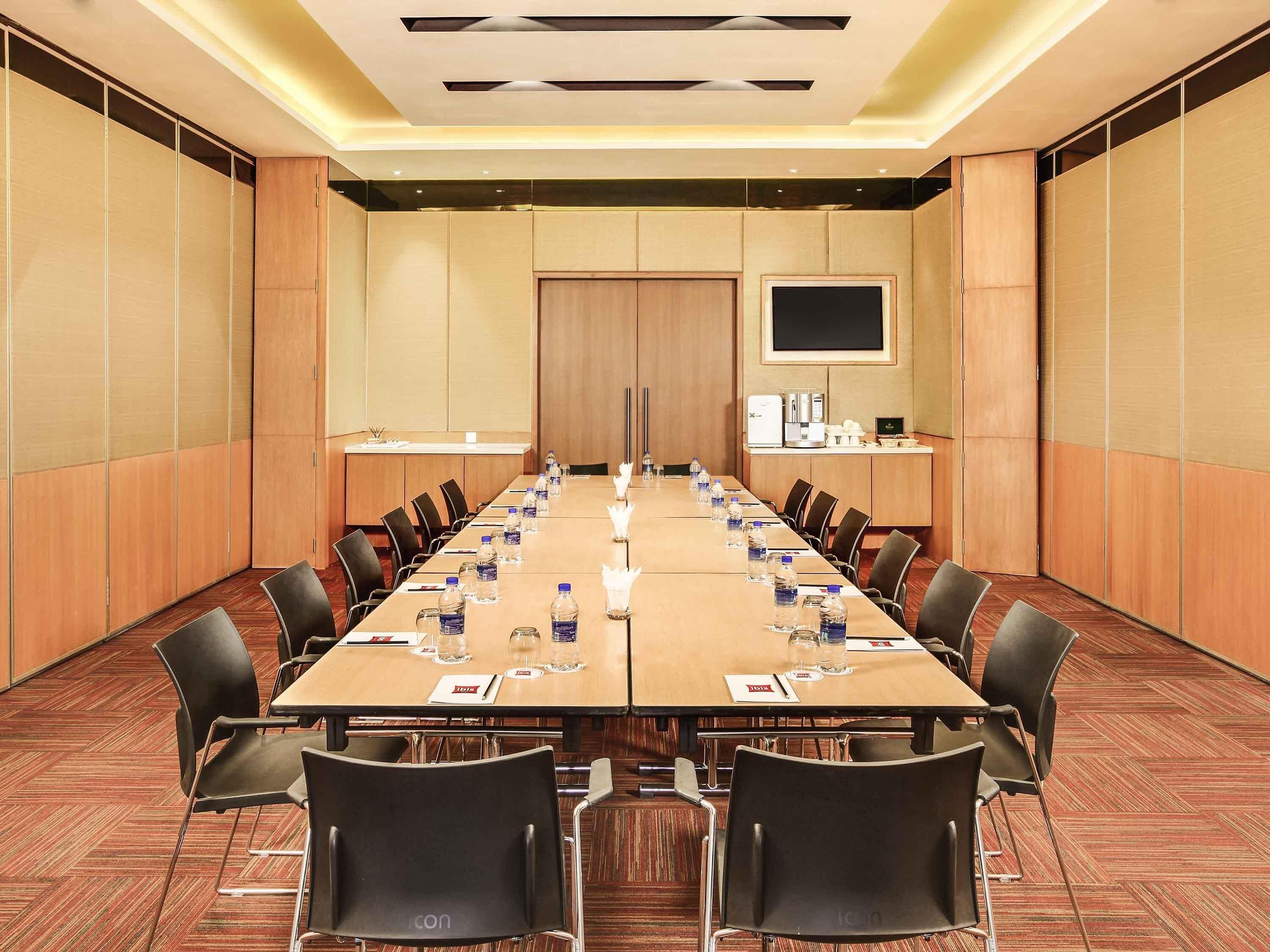 A conference room with a long table, chairs, water bottles, and a coffee machine.