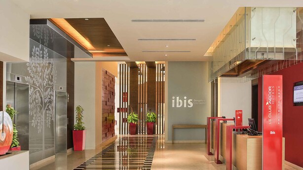 Un moderno vestíbulo de hotel con un mostrador de recepción, un área de atención al cliente y una escalera que conduce a un nivel superior.