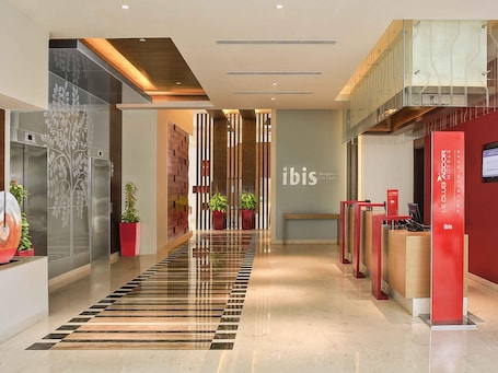 A modern hotel lobby with a check-in desk, a reception area, and a staircase leading to an upper level.. ibis Bengaluru City Centre Hotel