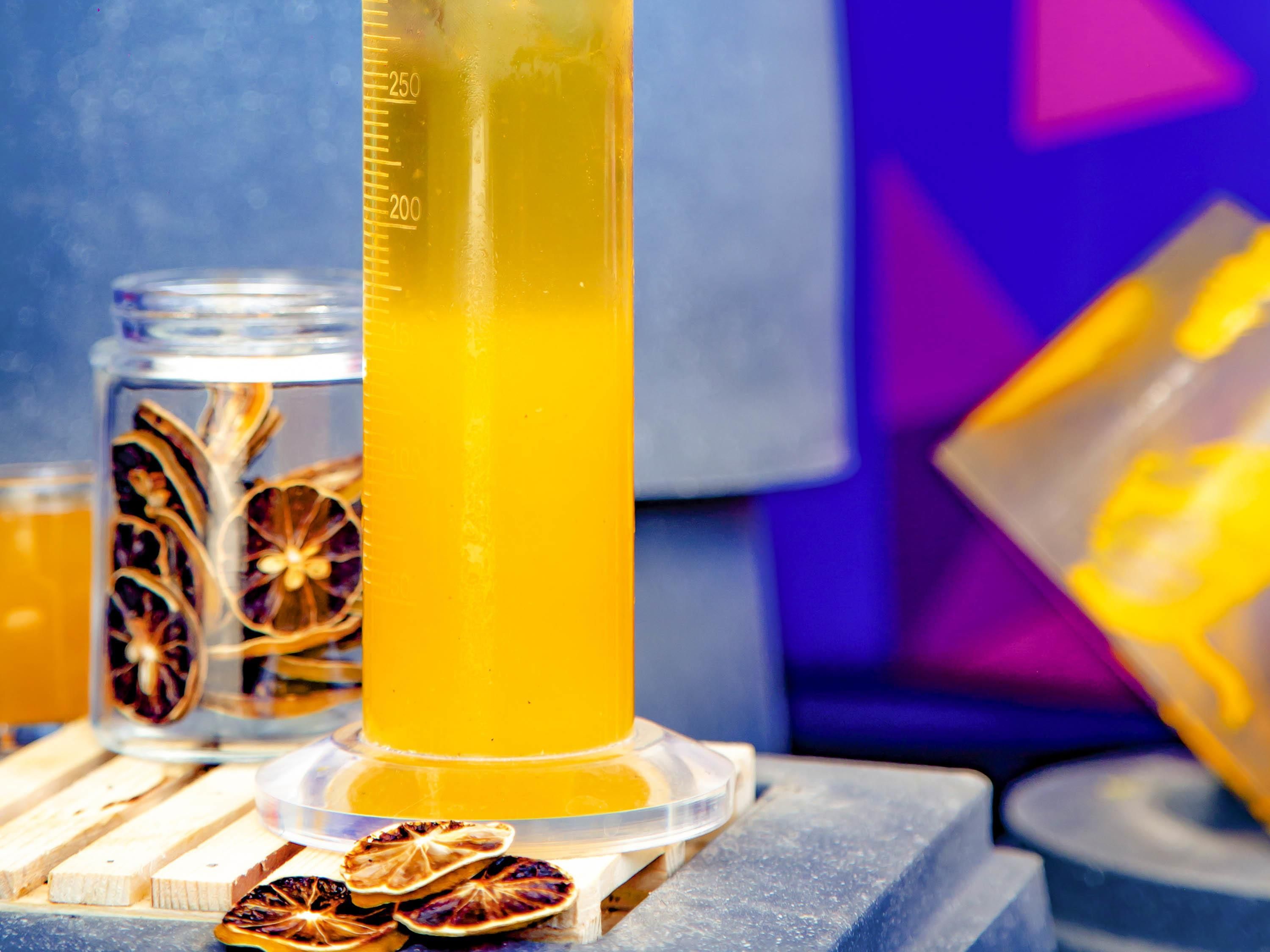 Un vaso alto con líquido amarillo, posiblemente una bebida, y rodajas de naranja deshidratada.