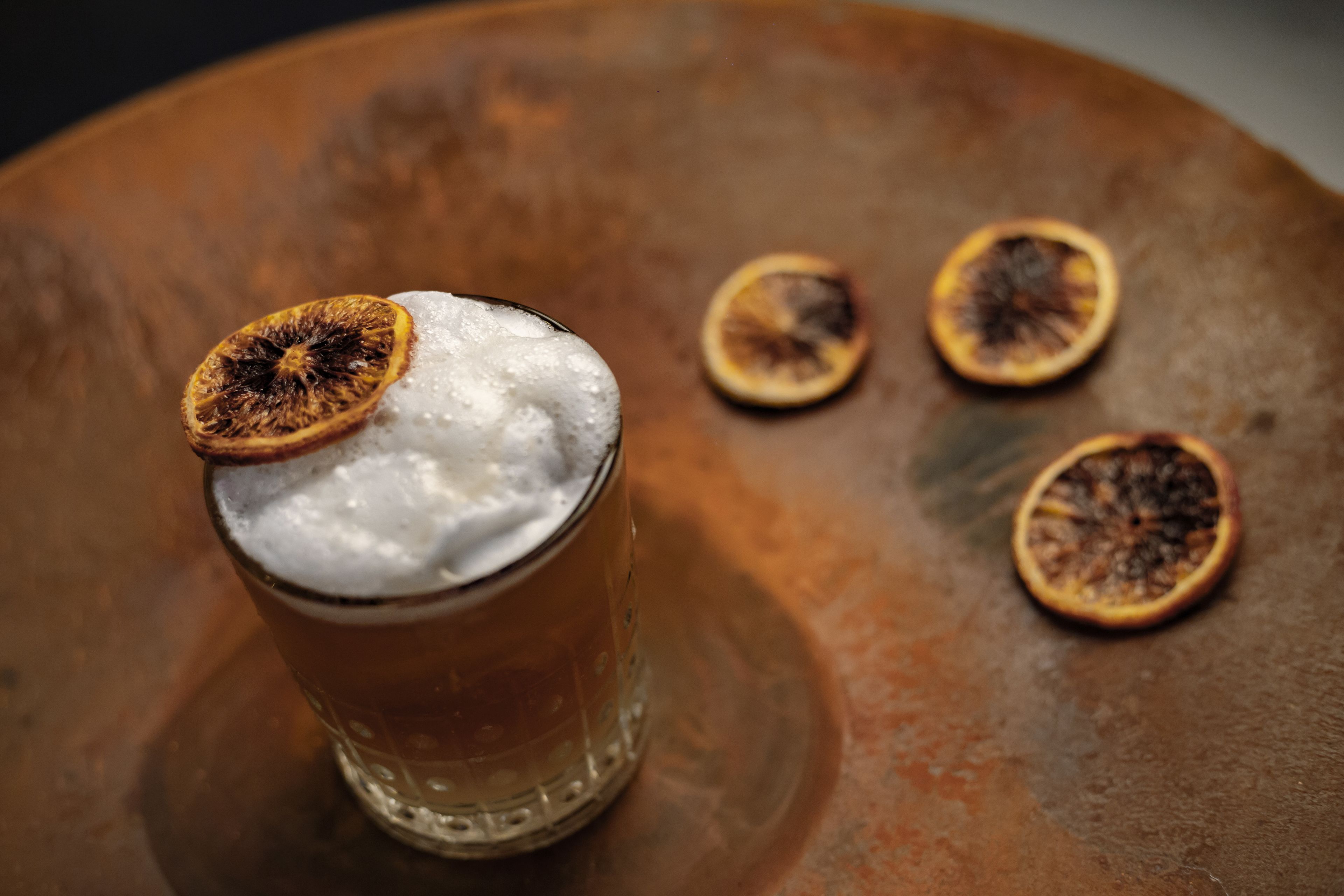 A glass with a frothy beverage and dried fruit garnish on a rustic table.